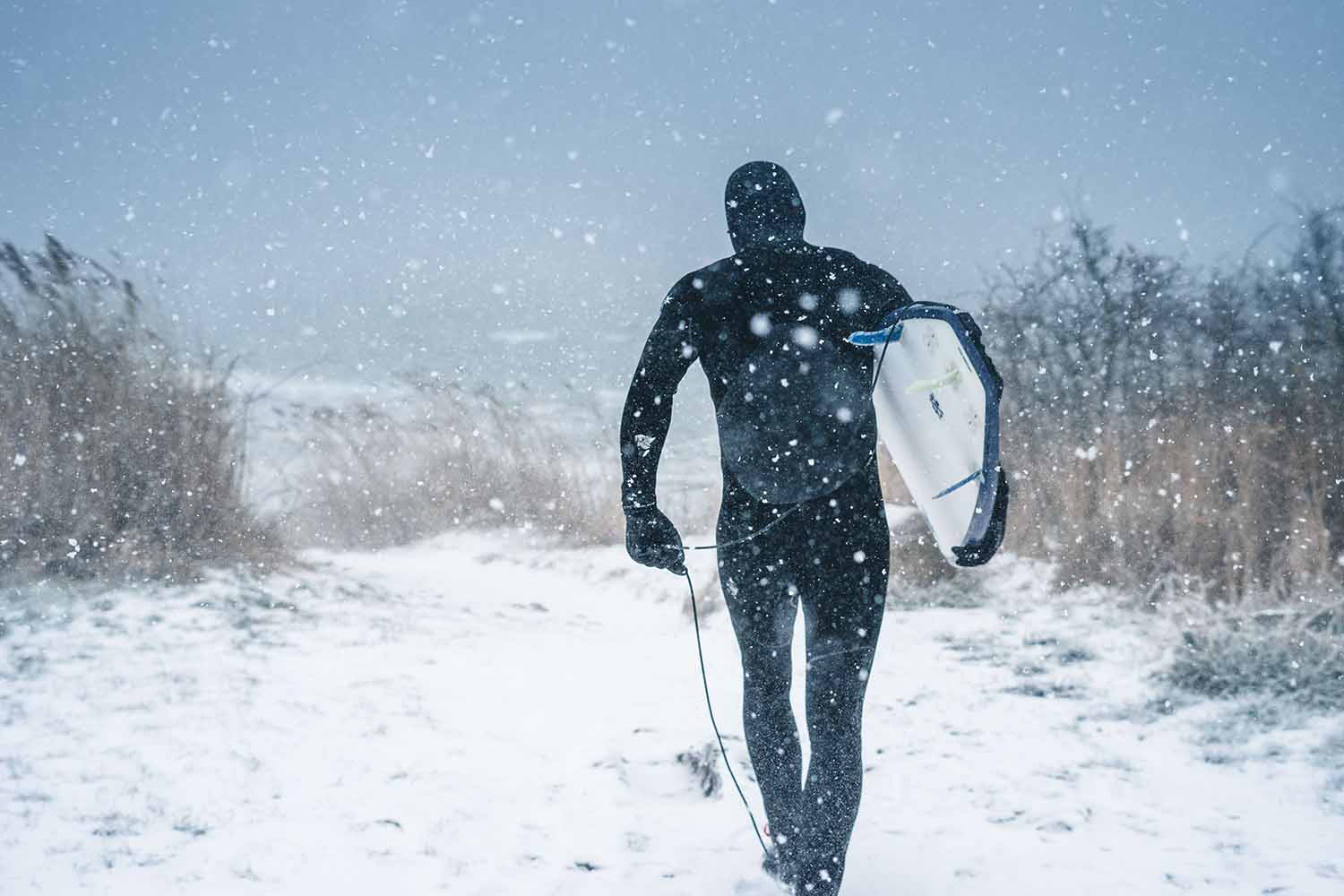 a person walking in the snow with a surfboard